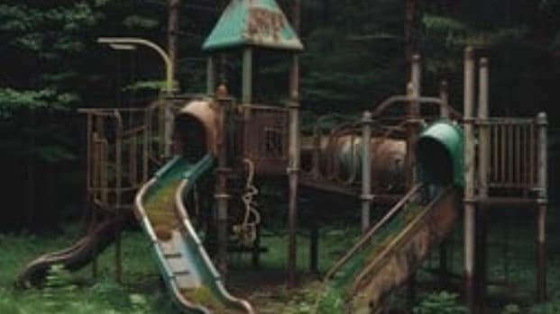 The image shows an abandoned playground. Apparently in the middle of the forest. In this context it is the abandoned Highland Park playground.